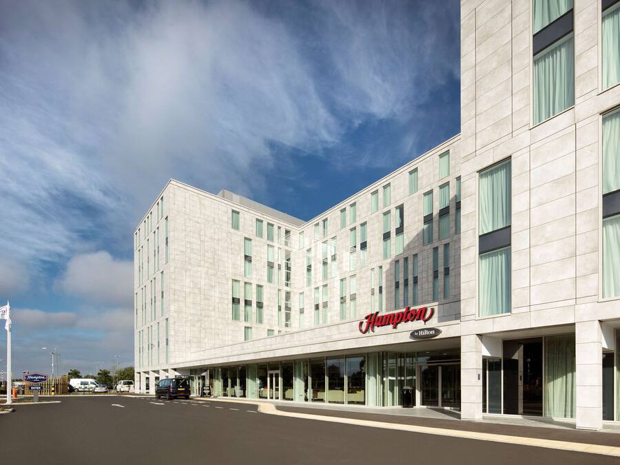 A modern hotel with a prominent Hampton sign, large windows, and a clean facade.