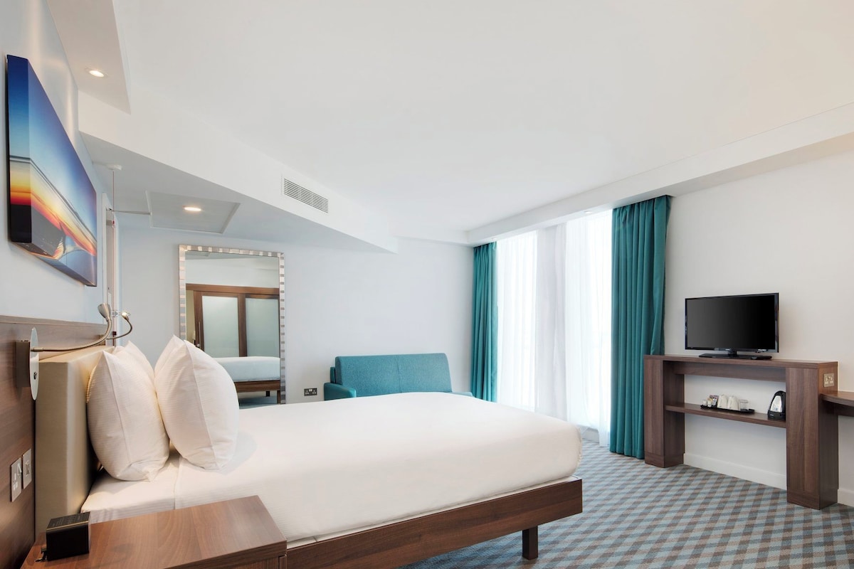 A hotel room with a large bed, a television, a desk, and a mirror.