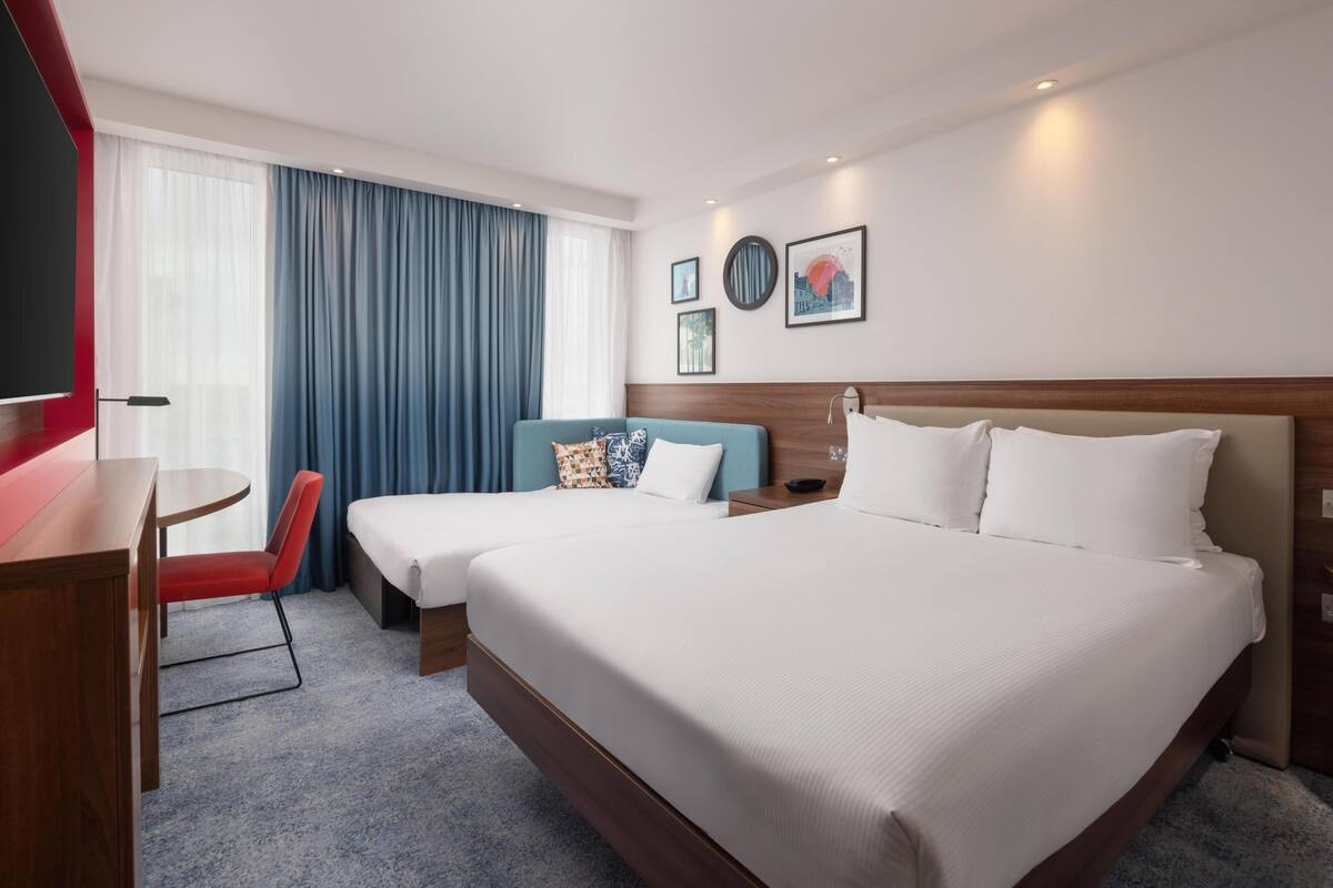 Habitación de hotel con dos camas, un escritorio, una silla, un televisor y una ventana con cortinas.