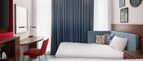 A hotel room with two beds, a desk, a chair, a TV, and a window with curtains.