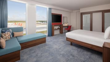 A hotel room with a large window, a sofa, a bed, a TV, and a desk.