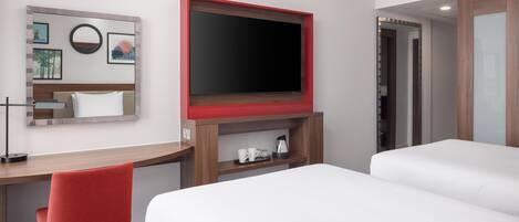 A hotel room with a bed, a desk with a chair, a TV mounted on the wall, and a mirror.
