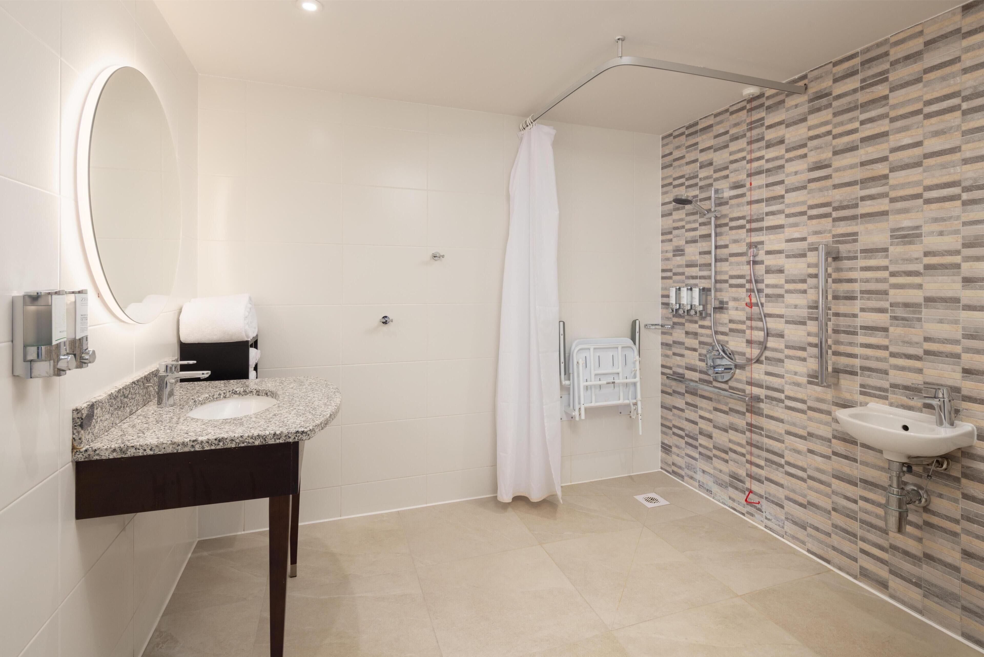 Ein modernes Badezimmer mit Granitwaschbecken, einem großen Spiegel, einer Dusche mit Glastür und einer gefliesten Wand.