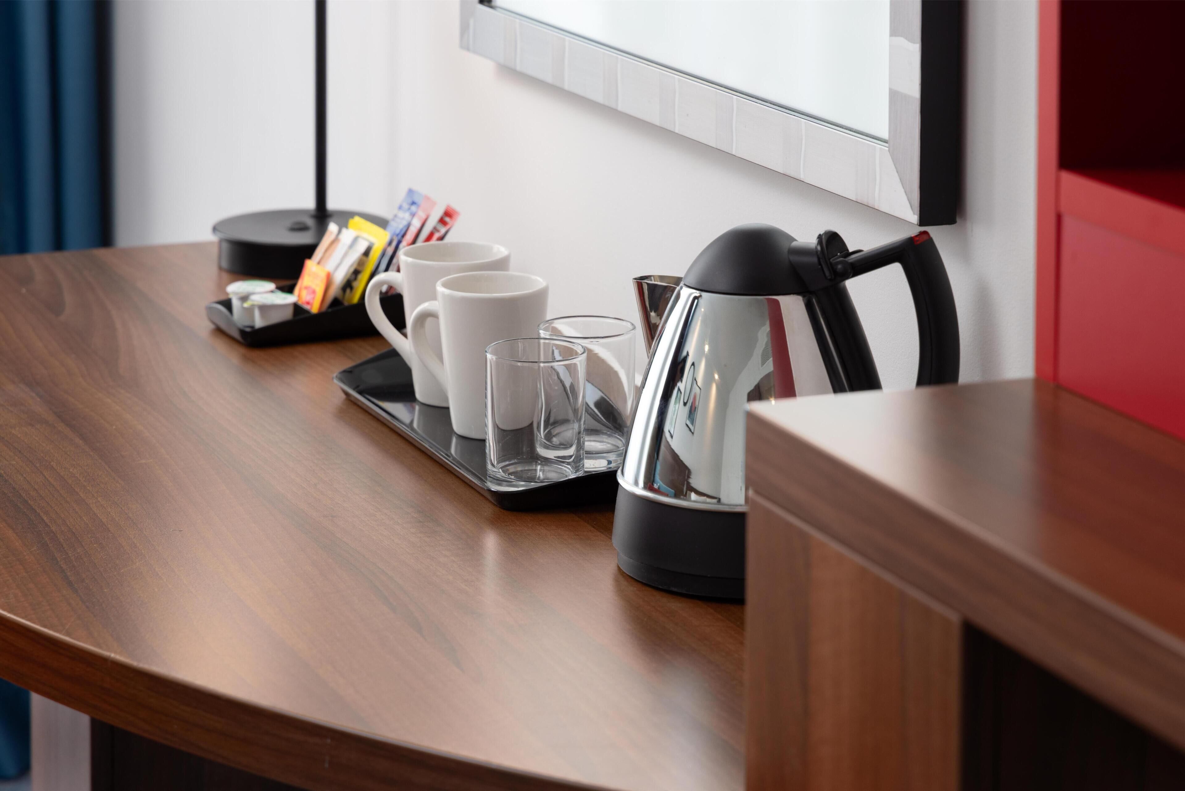 A wooden table with a tray holding a coffee maker, two white mugs, and two glasses.