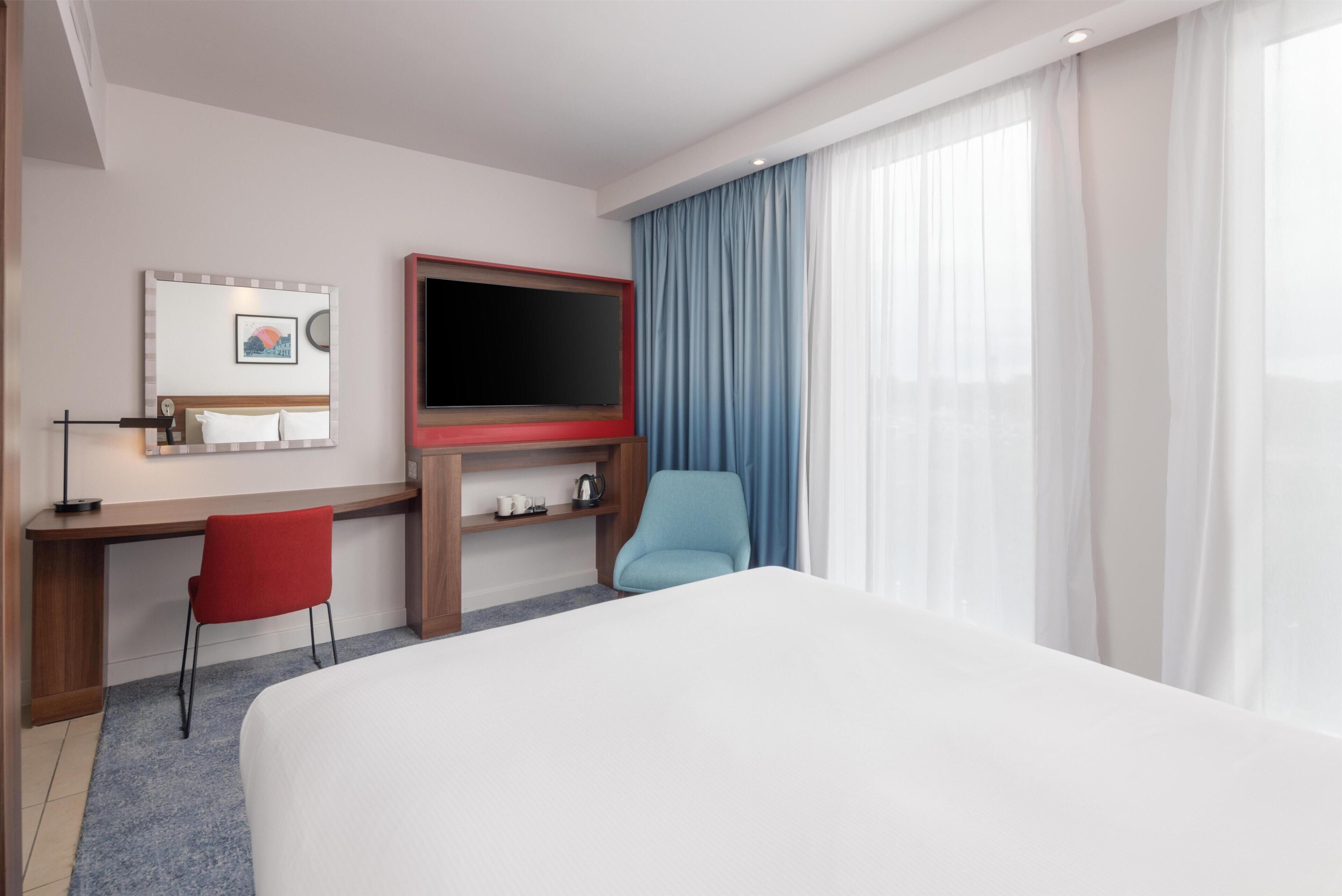 Een hotelkamer met een bed, een bureau met stoel, een televisie en een raam met gordijnen.