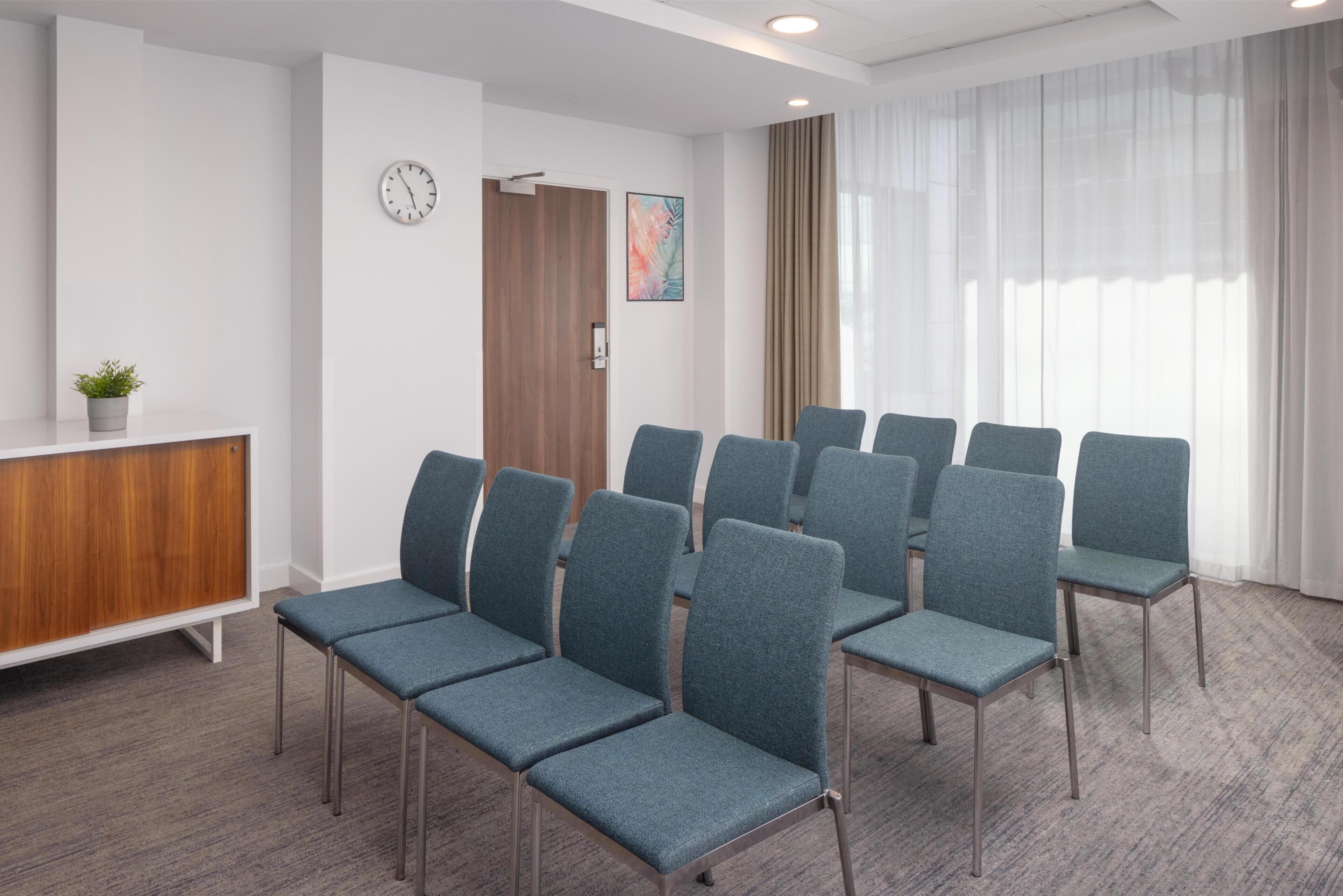 Un salón de conferencias con filas de sillas, un reloj, una planta y un armario de madera.