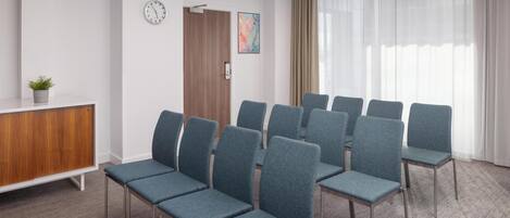 Un salón de conferencias con filas de sillas, un reloj, una planta y un armario de madera.
