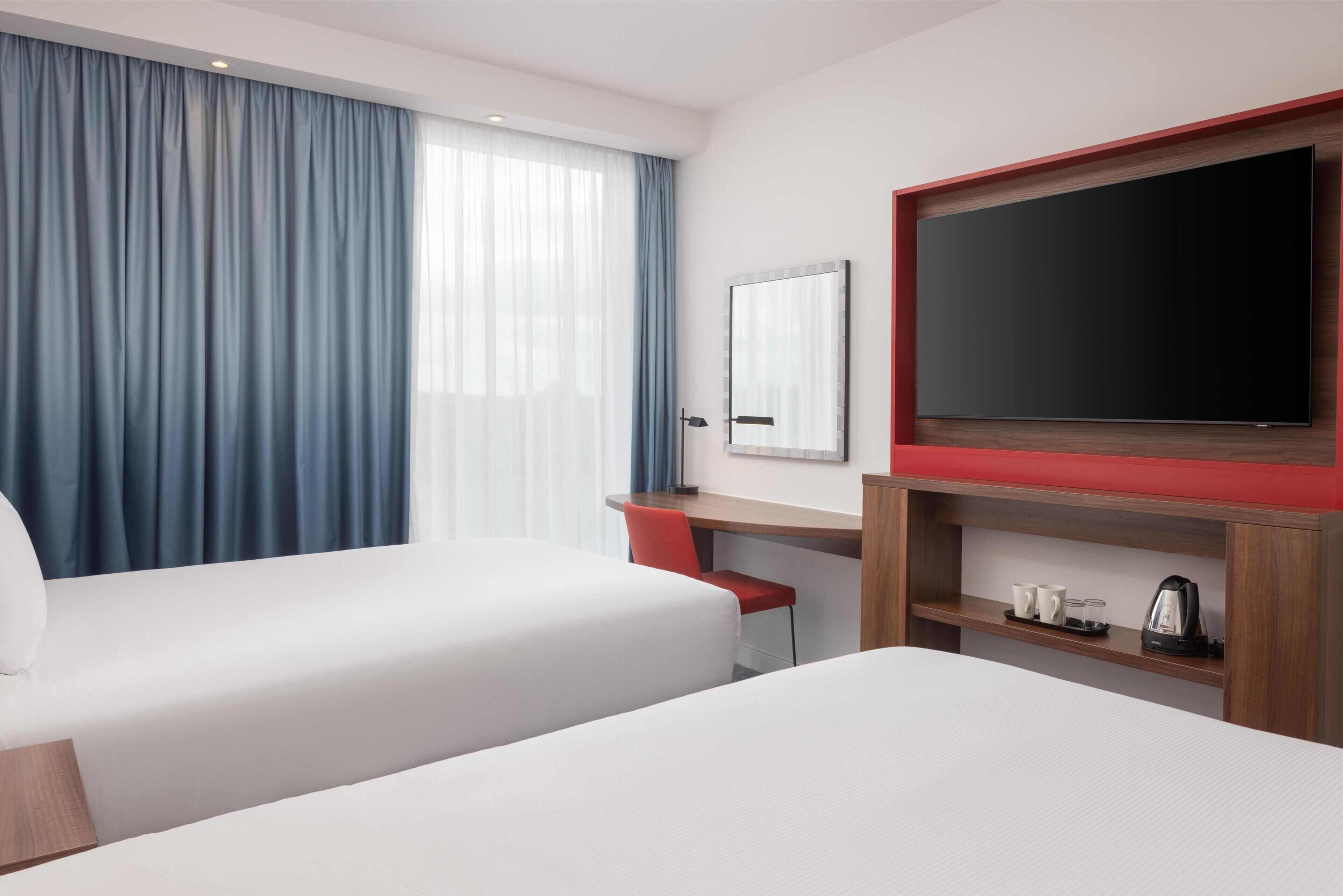 A hotel room with two beds, a desk, a chair, a TV, and a coffee maker.