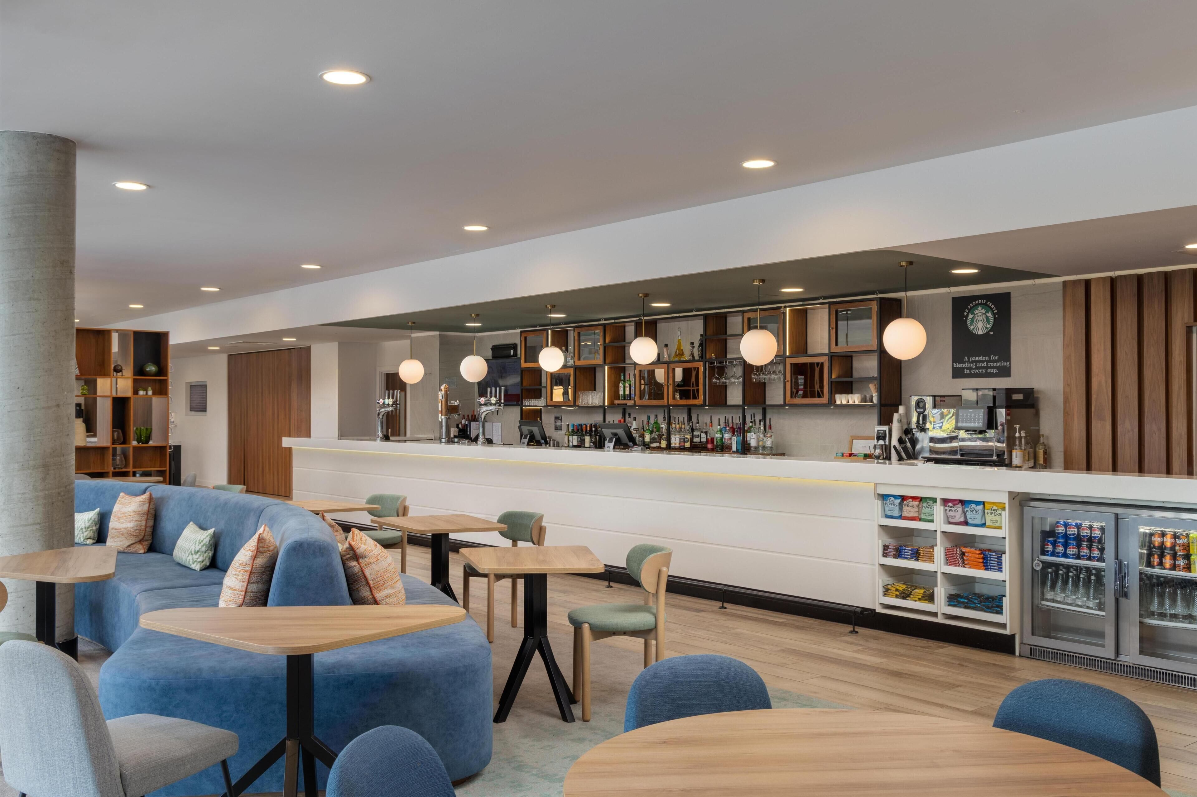 Un área de bar moderna con asientos, una barra y un refrigerador lleno de bebidas.