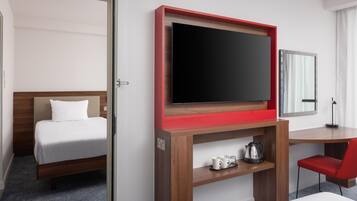 A hotel room with a bed, a TV on a wooden stand, a desk with a chair, and a mirror on the wall.