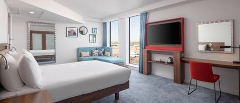 A hotel room with a bed, a sofa, a desk, a TV, and a large window.