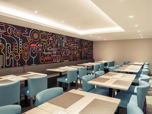 Ein moderner Essbereich mit blauen Stühlen und Tischen, einer schwarzen Wand mit farbenfroher abstrakter Kunst und Einbaustrahlen.