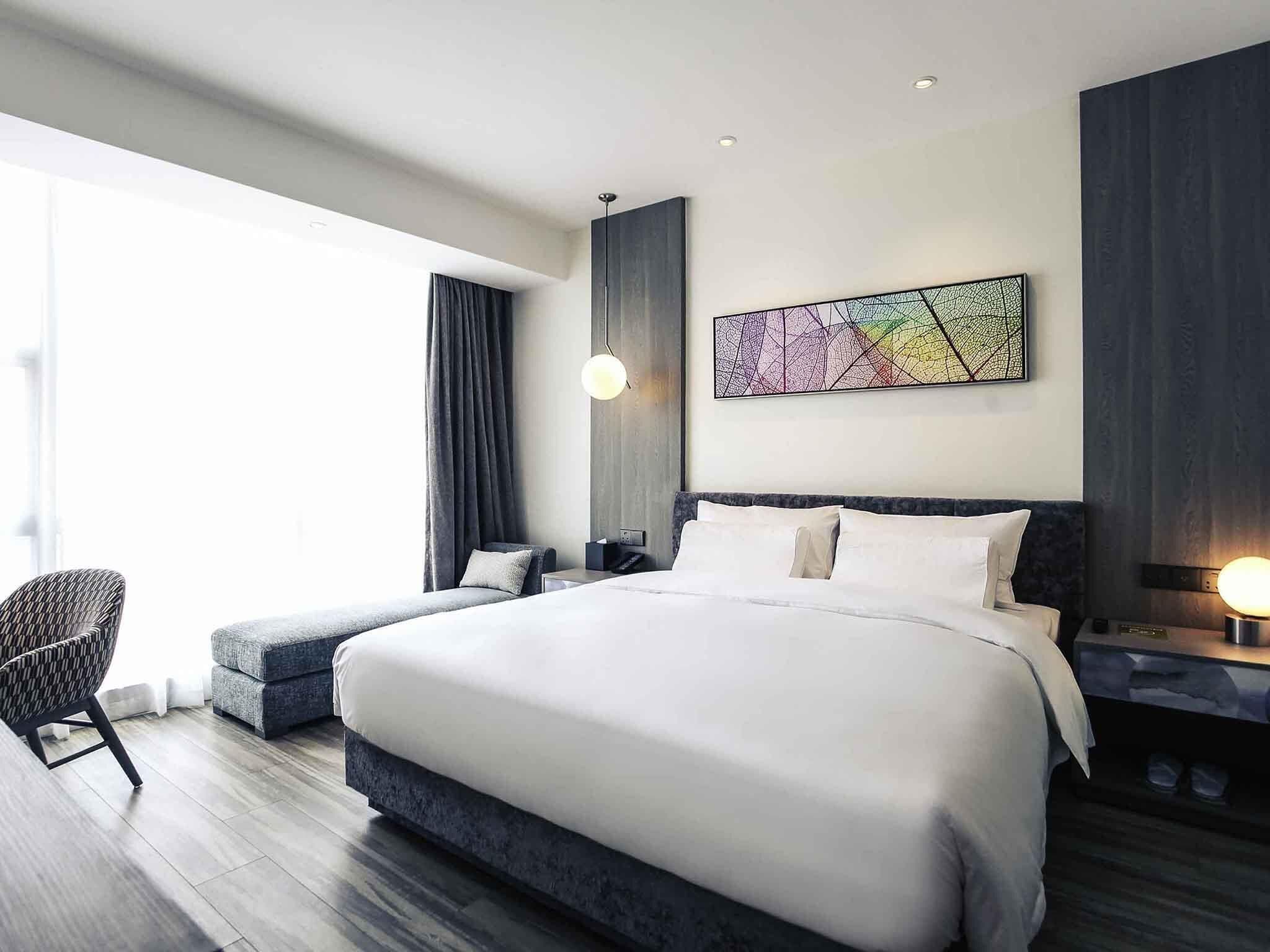 Une chambre d’hôtel moderne avec un grand lit, une chaise, une table de chevet et une œuvre d’art accrochée au mur.