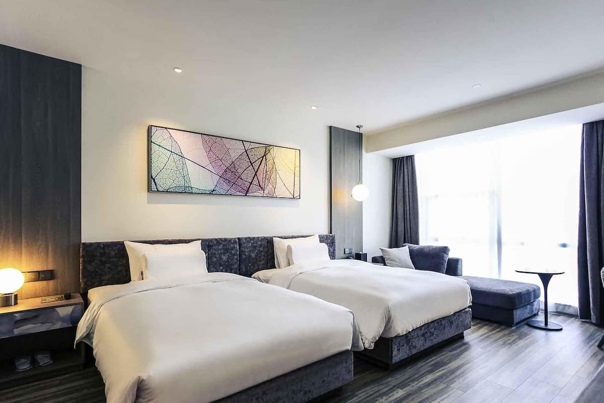 A modern hotel room with two beds, a large window, and a contemporary abstract painting.