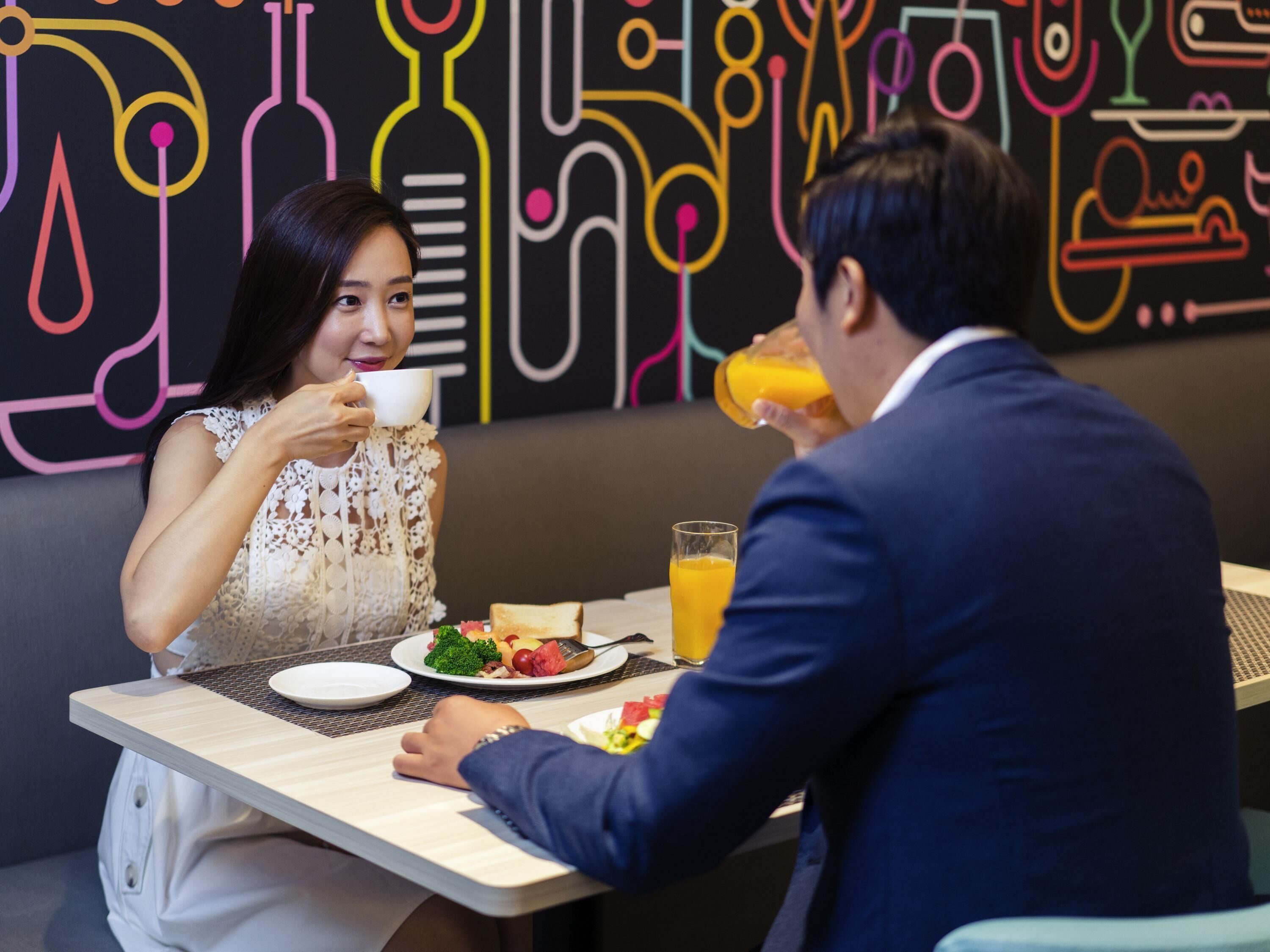 Un comedor con una mesa lista para dos personas, platos de comida y un vaso de jugo de naranja.