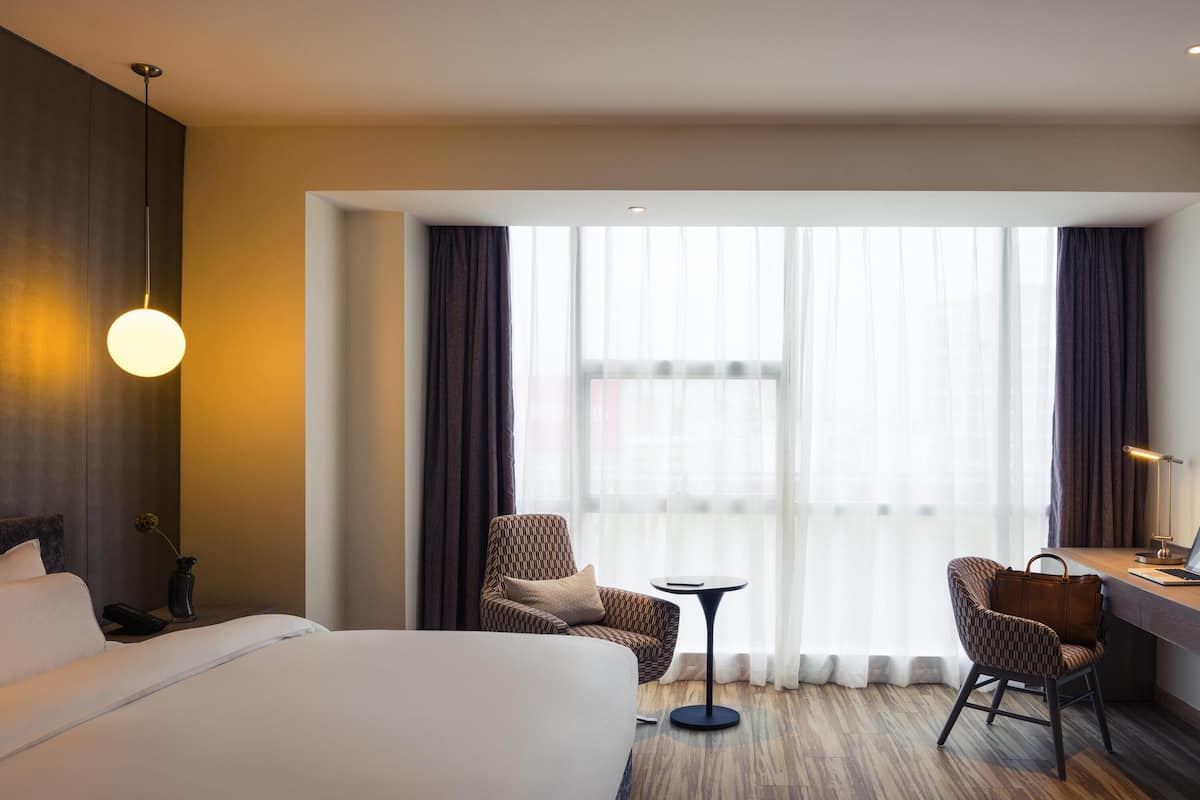 A hotel room with a large bed, two armchairs, a small round table, and a desk with a chair.