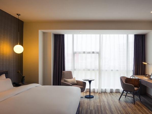Une chambre d’hôtel avec un grand lit, deux fauteuils, une petite table ronde et un bureau avec une chaise.