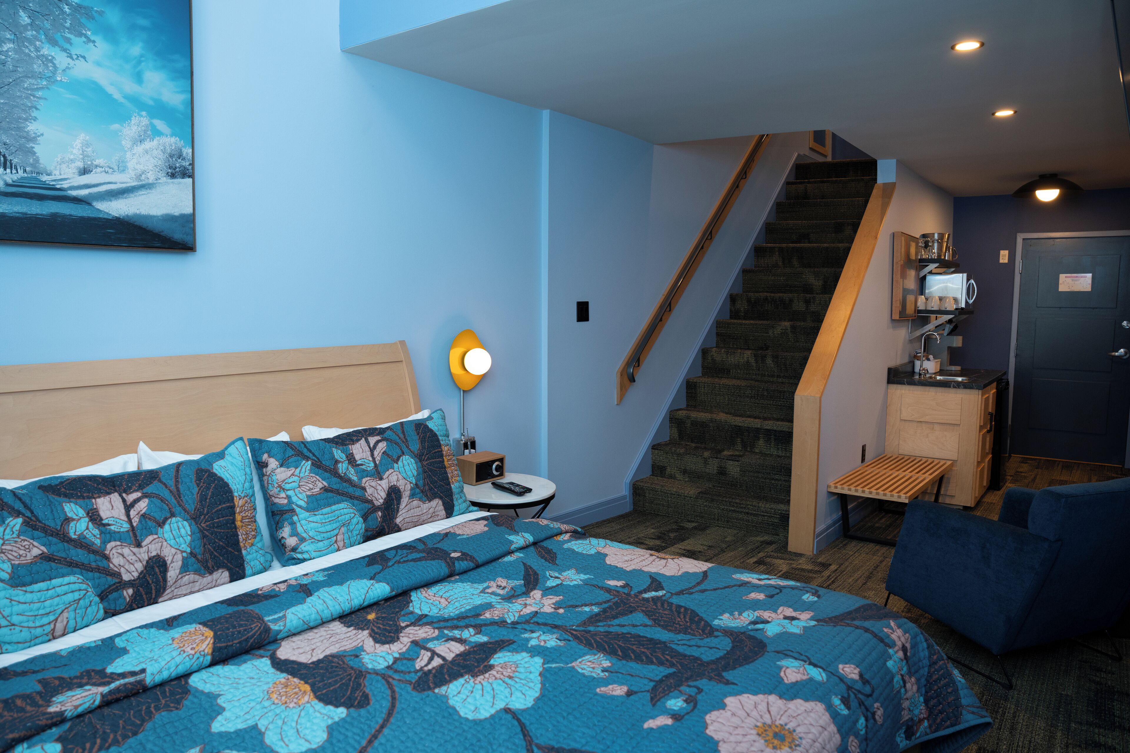 A bedroom with a bed, a nightstand, a lamp, a staircase, and a small table.