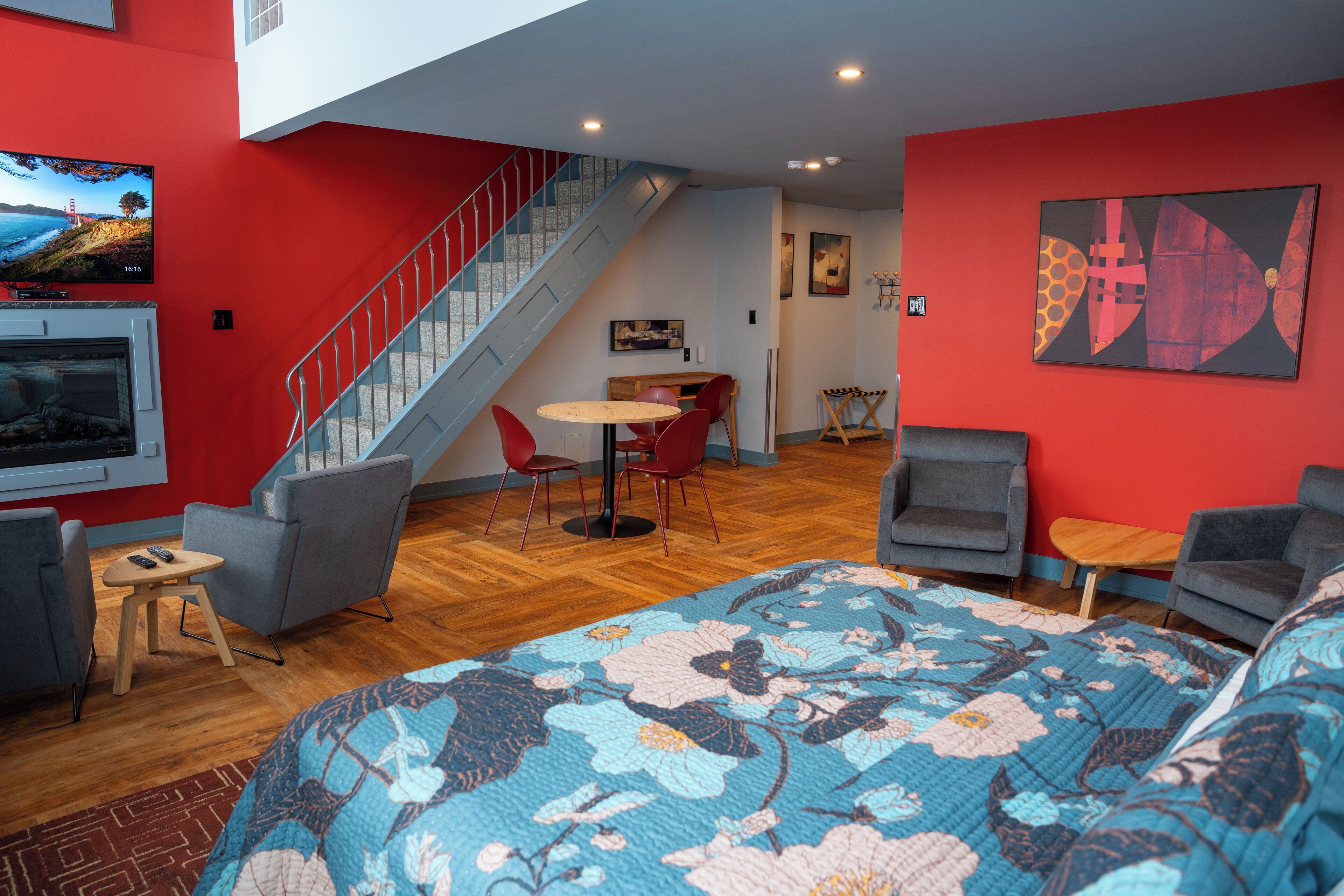 A modern hotel room with a large bed, a TV, a staircase, and a dining area.