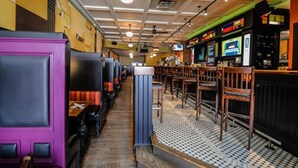 L’intérieur d’un restaurant avec des banquettes, des chaises en bois, un sol à motifs et un bar équipé d’écrans.