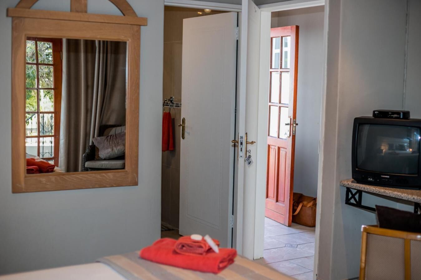 A hotel room with a bed, a television, a bathroom with a shower, and a door leading to another room.