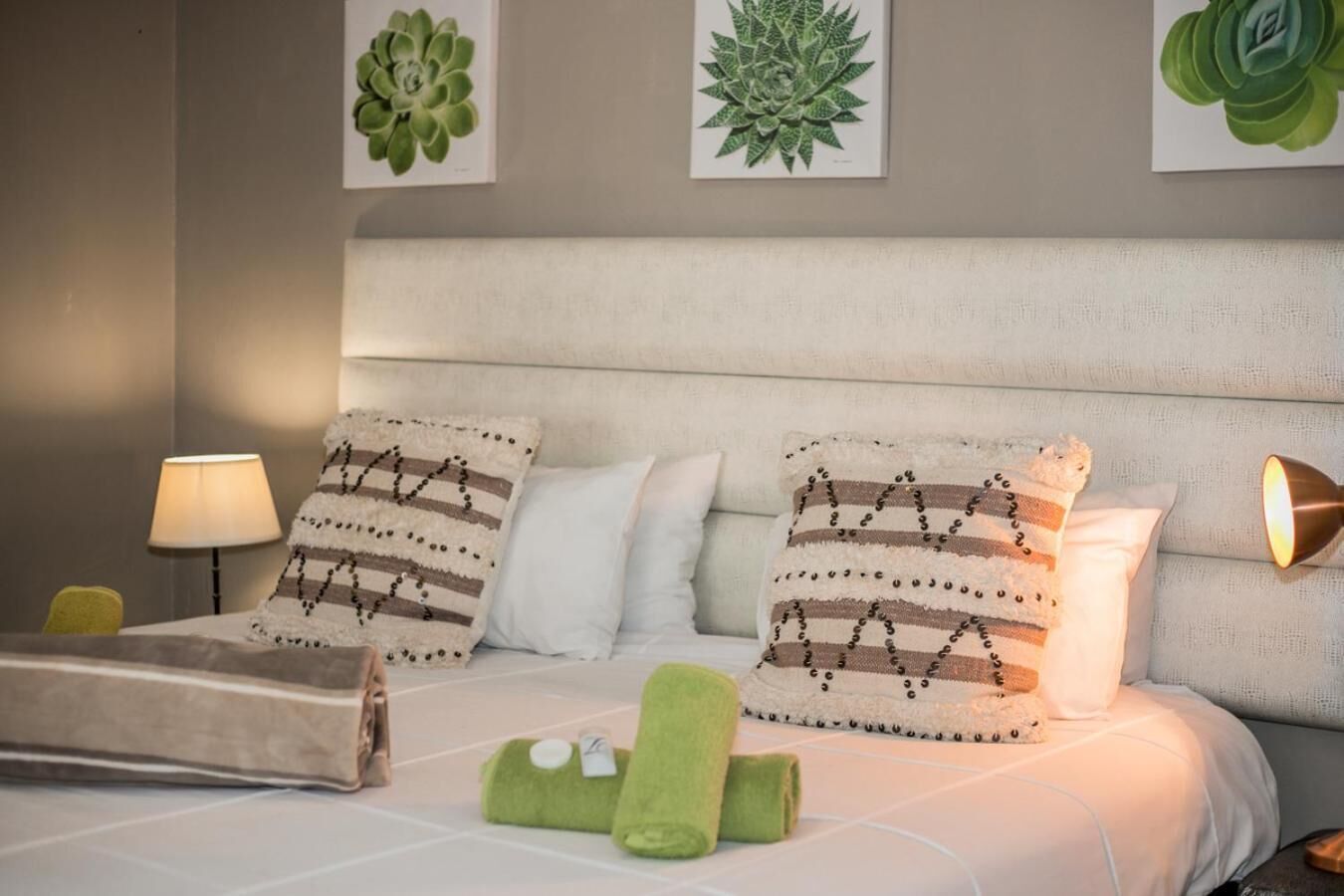 A neatly made bed with patterned pillows, a bedside lamp, and a green towel on the floor.