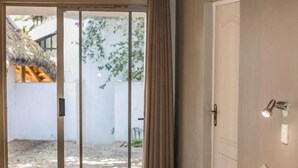 A bedroom with a bed, a bedside table, a window with curtains, a door, and a view of the outside.
