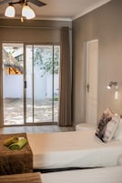 Un dormitorio con cama, mesita de noche, ventana con cortinas, puerta y vistas al exterior.