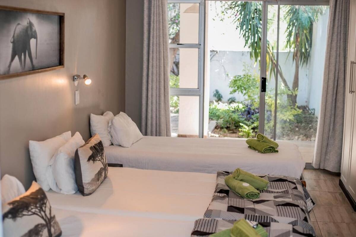 Ein Hotelzimmer mit zwei Betten, einem großen Fenster mit Blick auf Grünflächen und einem Bild an der Wand.