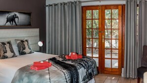A hotel room with a large bed, a desk, and a view through a glass door.