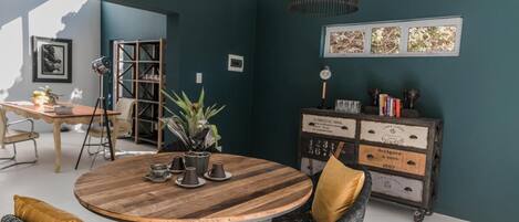 A dining area with a round wooden table, two chairs, a potted plant, and a vintage mail-themed cabinet.