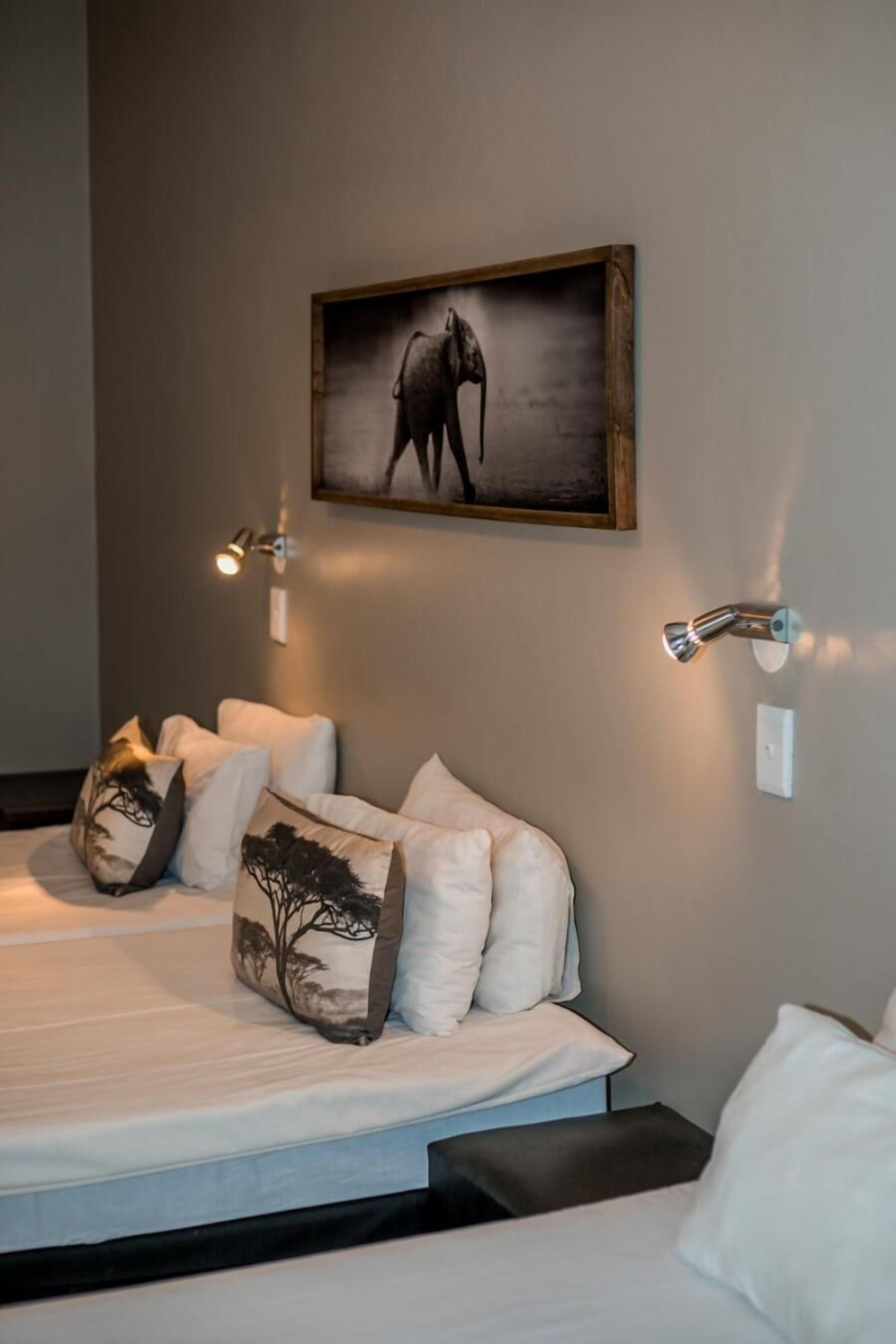 A bedroom with a bed, pillows, a wall-mounted picture, and two wall-mounted lights.
