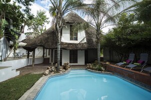 Un área junto a la piscina con una casa de techo de paja, sillas de descanso y una piscina pequeña.