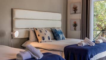A hotel room with a large bed, two bedside tables, a nightstand, and a window with a view of greenery.
