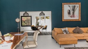 A modern living room with a brown sofa, a dining table with chairs, and a large window with a view of trees.