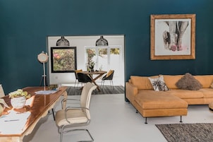 Una sala de estar moderna con un sofá marrón, una mesa de comedor con sillas y un ventanal con vistas a árboles.