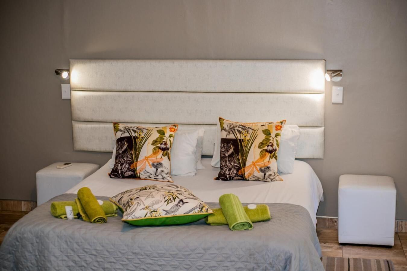 Un letto rifatto con cura, una testiera imbottita, due cuscini decorativi con motivo naturale e asciugamani arrotolati sul letto.