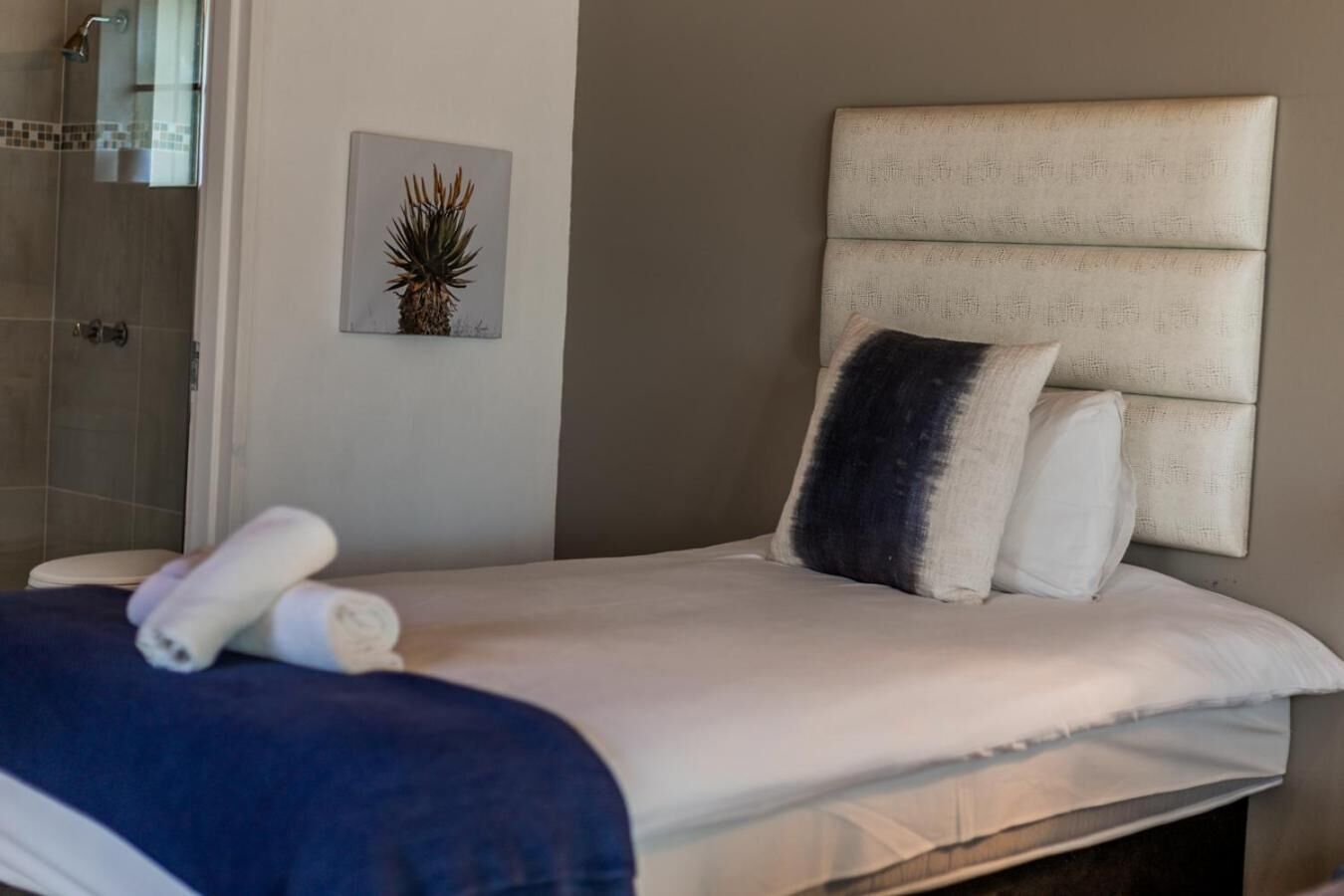 A neatly made bed with a headboard, a towel, and a framed picture of a plant on the wall.