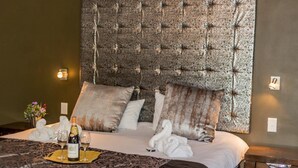 Una cama bien hecha con una colcha estampada, una botella de champán y una copa en una bandeja.