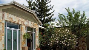 Un edificio con fachada de piedra, amplias ventanas y un jardín con plantas en flor.