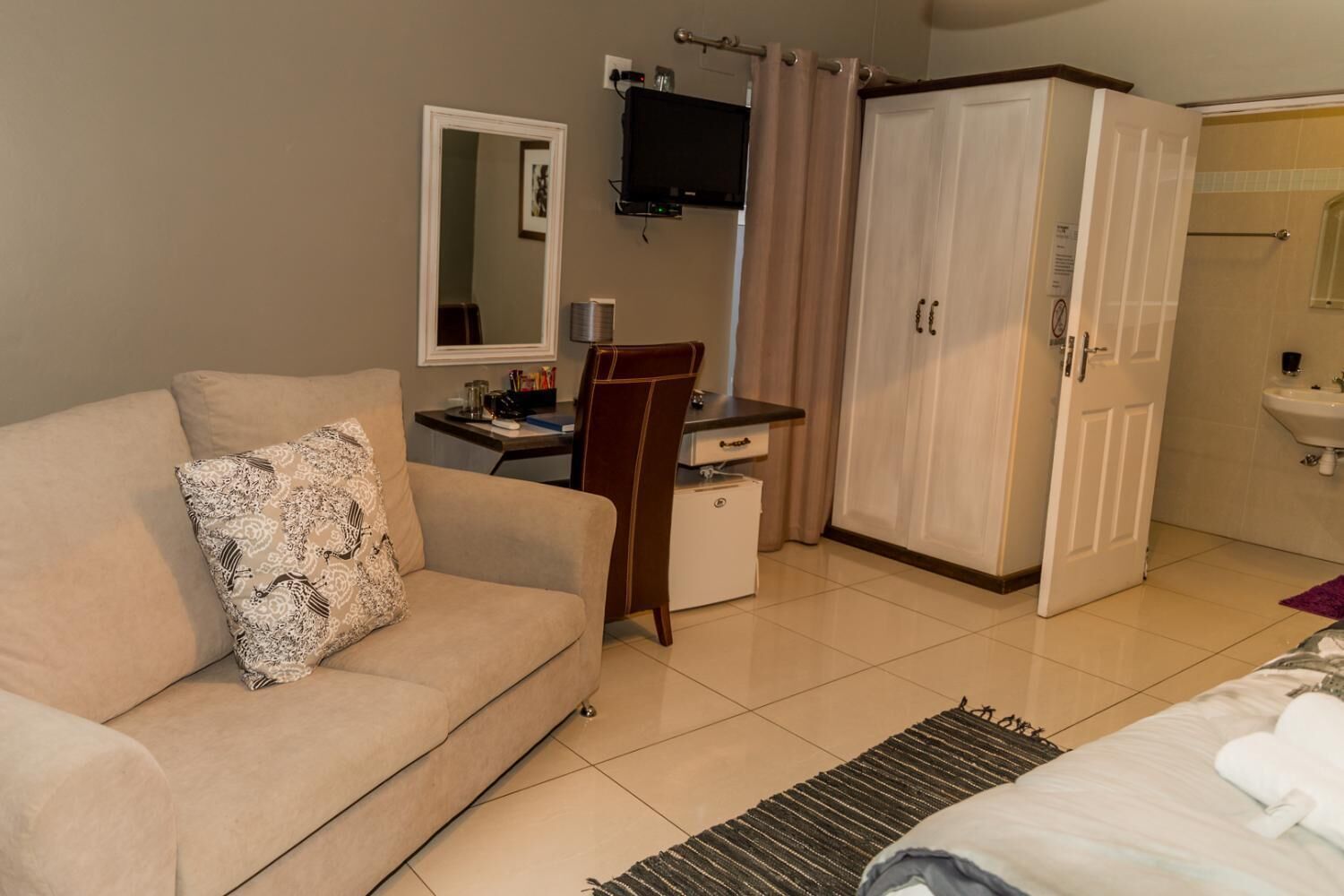 A hotel room with a sofa, a desk, a wardrobe, and a bathroom.