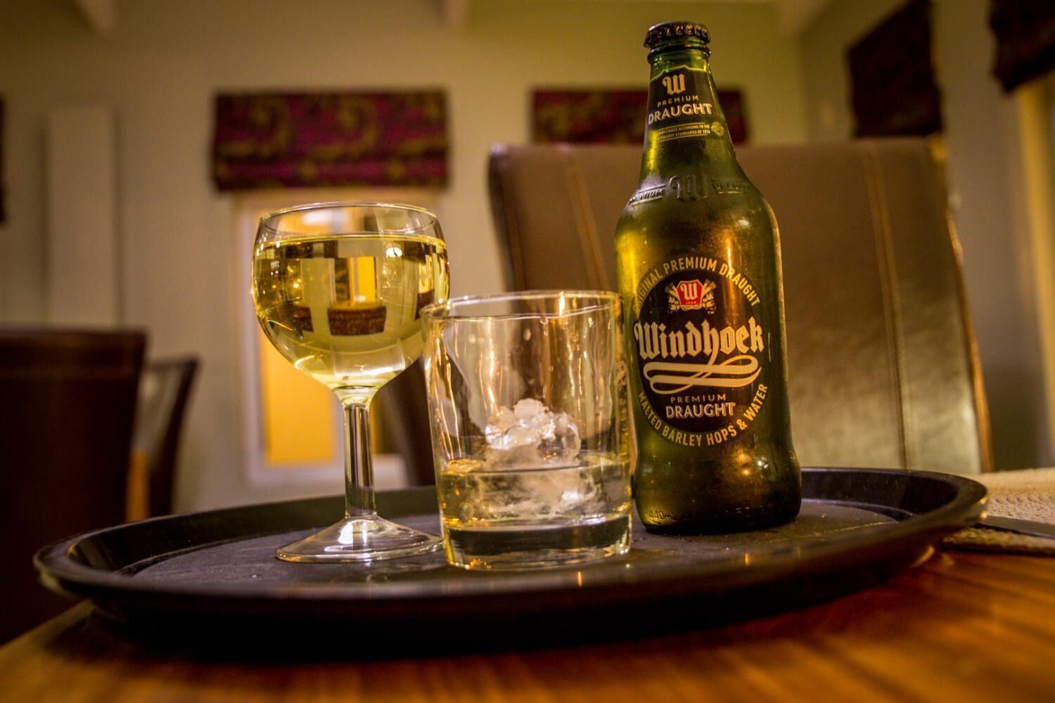 Uma garrafa de cerveja Windhoek Premium Draught, um copo de cerveja e um copo com cubos de gelo em um tabuleiro.