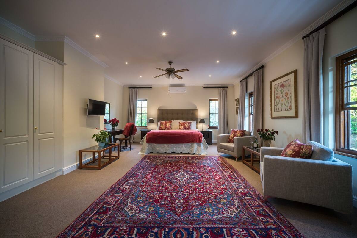 Een ruime slaapkamer met een groot bed, een plafondventilator en uitzicht op de omgeving door een raam.
