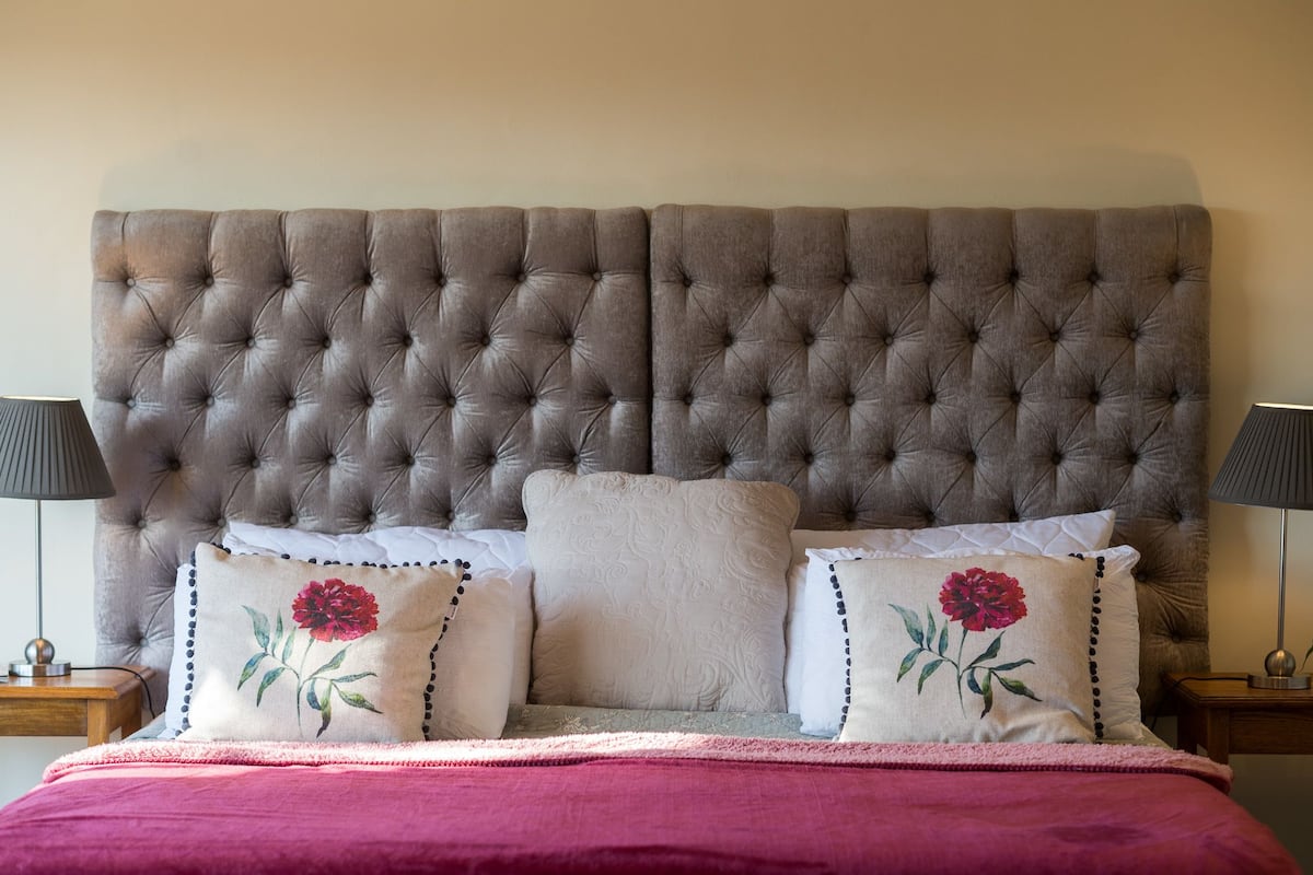 Een slaapkamer met een gestoffeerd hoofdeinde, een bed met een roze deken en twee bedlampjes.