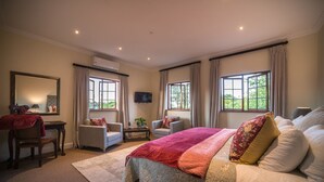 Een ruime slaapkamer met een groot bed, twee fauteuils, een bureau en een televisie.