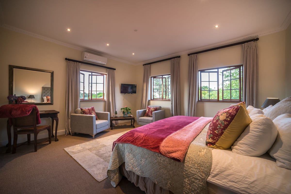 Een ruime slaapkamer met een groot bed, twee fauteuils, een bureau en een televisie.