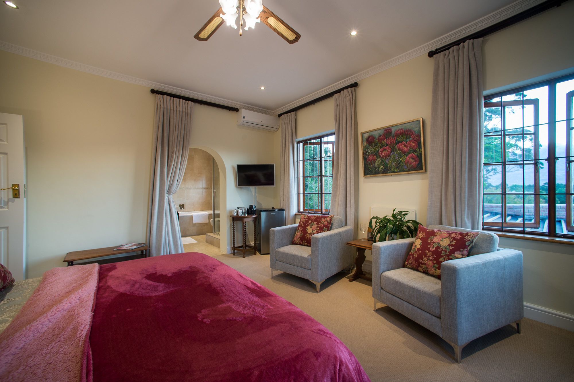 A hotel room with a bed, two armchairs, a small table, a TV, and a painting.