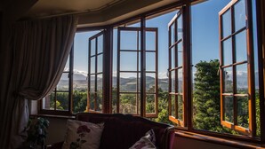 Een kamer met een groot erkerraam met uitzicht op een groen landschap en heuvels in de verte.