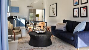 Ein modernes Wohnzimmer mit einem dunkelblauen Sofa, einem runden schwarzen Couchtisch und einem Essbereich mit Holztisch und Stühlen.