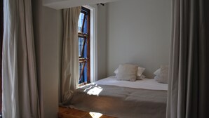 Ein Schlafzimmer mit einem Einzelbett, einem Fenster mit Vorhängen und einem Holz-Kopfteil.